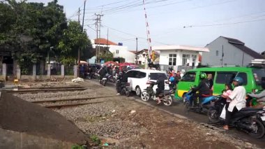 Bandung, Endonezya - 7 Ocak 2026. Motosikletliler ve yayalarla dolu işlek bir demiryolu. Trenlerin şehir alanından geçmesini bekliyorlar..