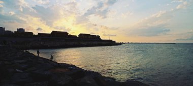 Romanya 'nın Köstence kentindeki Three Slippers Beach' te (Rumence; Plaja trei papuci) dalgalar. Yazın günbatımında dalgakırandan şehrin manzarası.