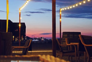 Romanya 'nın Köstence kentindeki Mamaia plajında gün batımında bir restoranın terası. Masalar, sandalyeler ve ışıklandırma ekipmanları kumsaldaki kumların yanında..