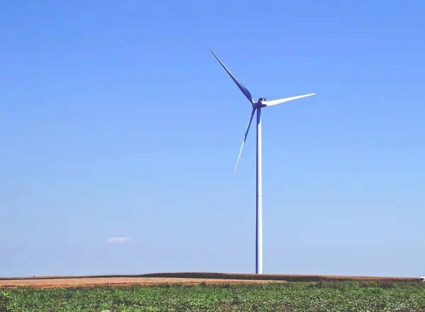 Electric wind turbine between farm fields in Romania. Wind turbine with a blue sky in the background.