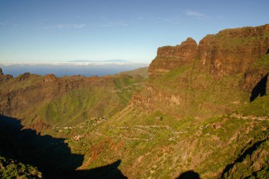 İspanya 'nın Kanarya Adaları, Tenerife Adası' ndaki Masca vadisine (kanyon) uzanan kıvrımlı yol. Ufuktaki La Palma adası Atlantik Okyanusu 'ndaki bulutlarla çevrili..