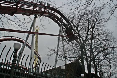 Kopenhag 'daki Tivoli eğlence parkının cazibesi. Bir ağacın dalları ve bulutlu gökyüzü arasında aşağıdan görülen hız treni. Danimarka.