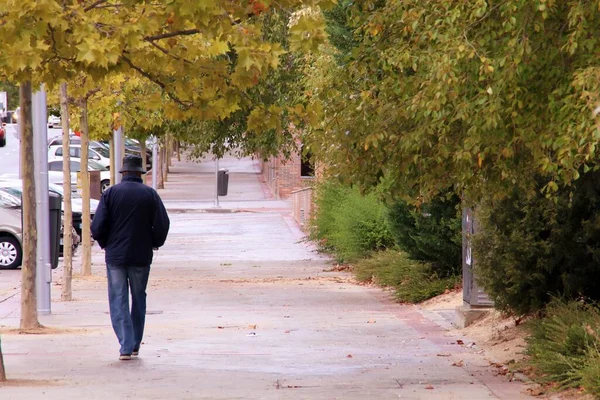 A man walking along Monasterio de Silos avenue, Madrid, Spain. Older man with rain hat walking down the sidewalk seen from behind.