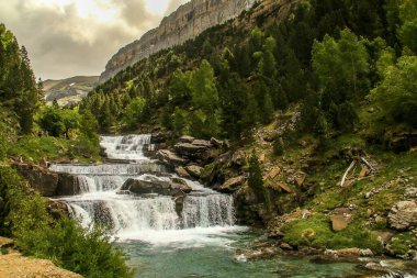 Soaso waterfall (also known as Soaso Steps) in Arazas river, the Pyrenees, Huesca, Spain. A beautiful natural landscape of the pine forest on the slopes of the mountain in early summer. clipart