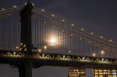 Brooklyn 'den Manhattan Köprüsü' ne. Ay, New York, ABD 'deki ünlü asma köprünün kablolarının arkasında parlıyor..