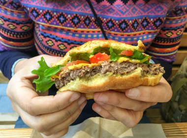 Yarısı yenmiş bir hamburgeri tutan eller. Domates ve marullu bir çizburger. New York restoranında servis edildikten sonra ısırılmış..
