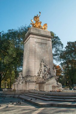 Güneşli bir günde New York 'taki Central Park' ın sonbahar şehri. Altın bir heykelle taçlandırılan USS Maine Ulusal Anıtı Central Park 'ın güneybatı girişinde duruyor. Kasım 2019.
