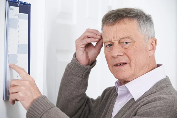 Запутавшийся пожилой человек со слабоумием, смотрящий на календарь — стоковое фото