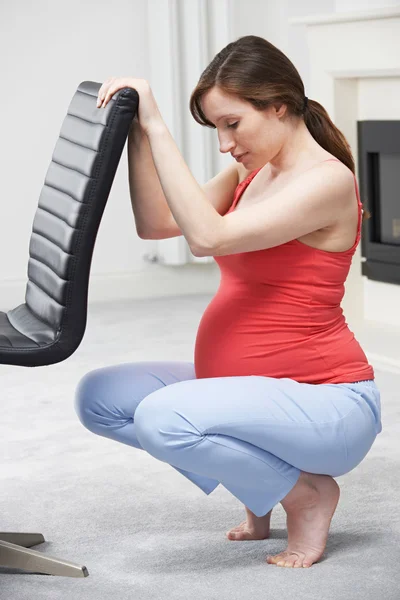 Kobieta w ciąży ćwiczenia przy użyciu tyłu fotel w domu — Zdjęcie stockowe