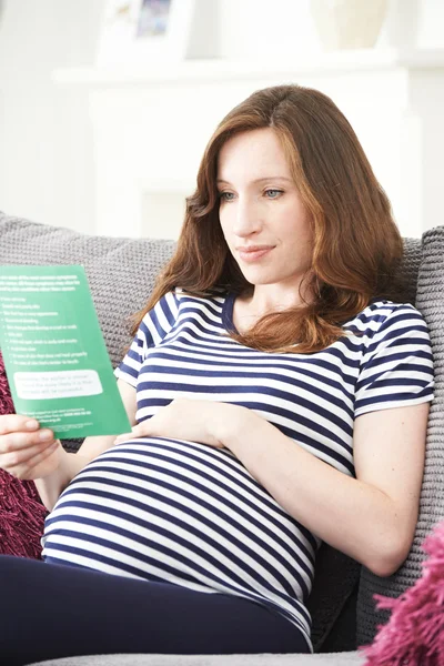 Беременная женщина читает брошюру с медицинским советом — стоковое фото