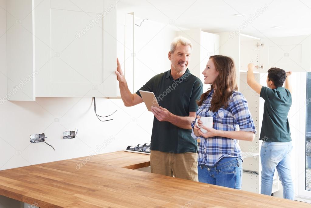 Woman With Carpenter Looking At Plans For Kitchen On Digital Tab