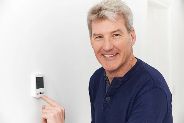 Sonriente hombre que ajusta el termostato en el sistema de calefacción del hogar — Foto de Stock