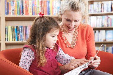 Mother And Daughter Reading Book In Library clipart
