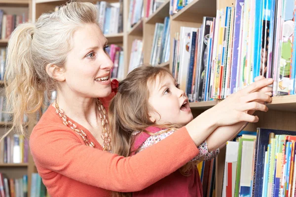 Mor och dotter att välja bok från biblioteket hylla — Stockfoto