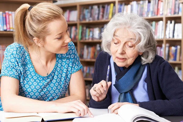 Старшая женщина работает с учителем в библиотеке — стоковое фото