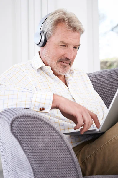 Reifer Mann streamt Musik vom Laptop auf drahtlose Kopfhörer — Stockfoto