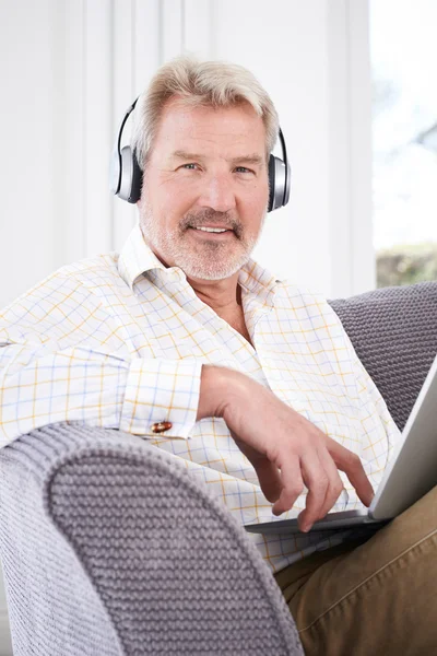 Reifer Mann streamt Musik vom Laptop auf drahtlose Kopfhörer — Stockfoto