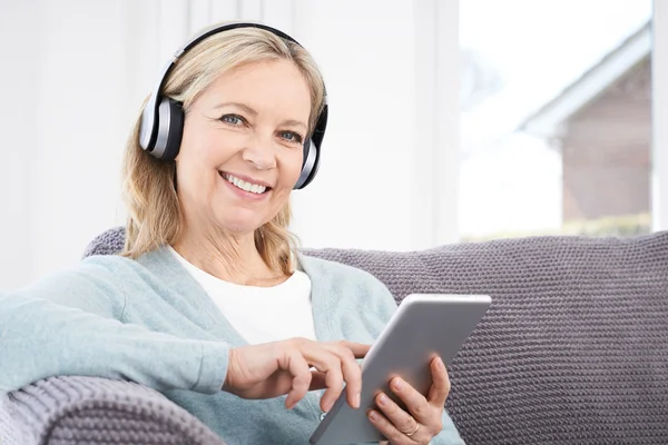 Mogen kvinna strömmar musik från Digital Tablet till trådlös Headp — Stockfoto