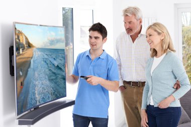 Man Demonstrating New Television To Mature Couple At Home clipart