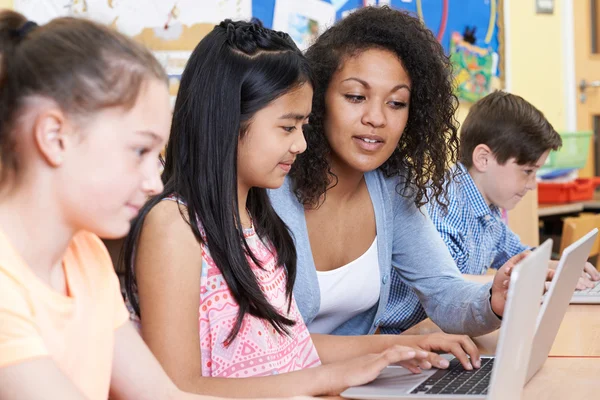 Teacher Helping Group of Elementary School Children In Computer — стоковое фото
