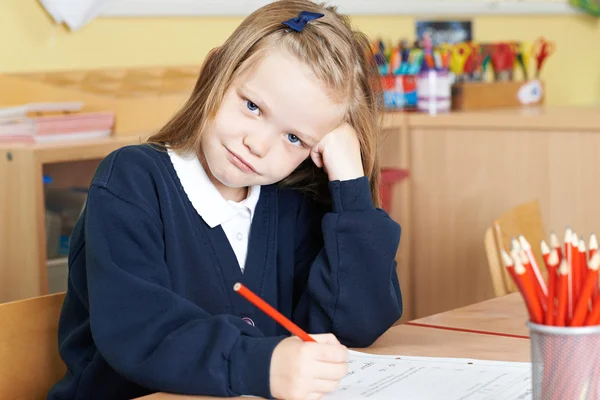 Скучная ученица начальной школы за столом — стоковое фото