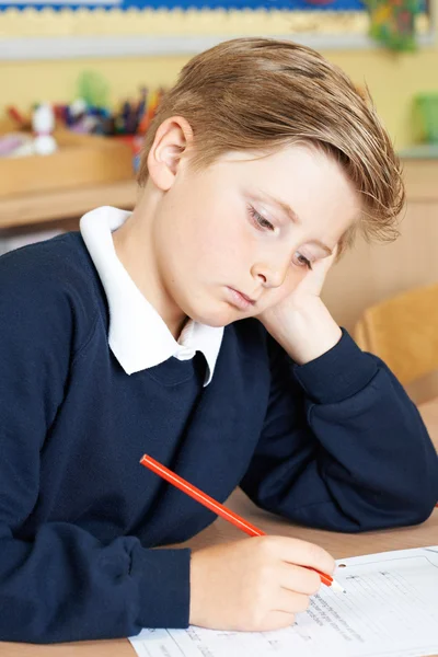 Скучный ученик начальной школы за столом — стоковое фото