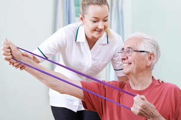 Physiotherapist Helping Senior Male To Use Resistance Band — Stock Photo, Image