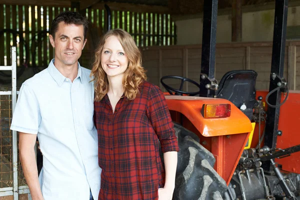 Ritratto di coppia di agricoltori in piedi in fienile con trattore — Foto Stock