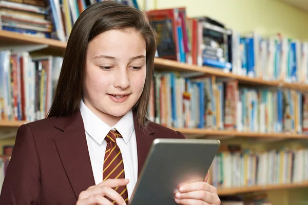 Chica vistiendo uniforme escolar usando tableta digital en la biblioteca —  Fotos de Stock