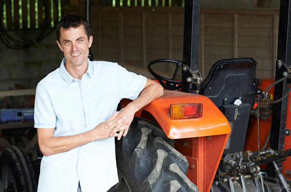 Portrait Of Farmer Standing In Barn With Tractor