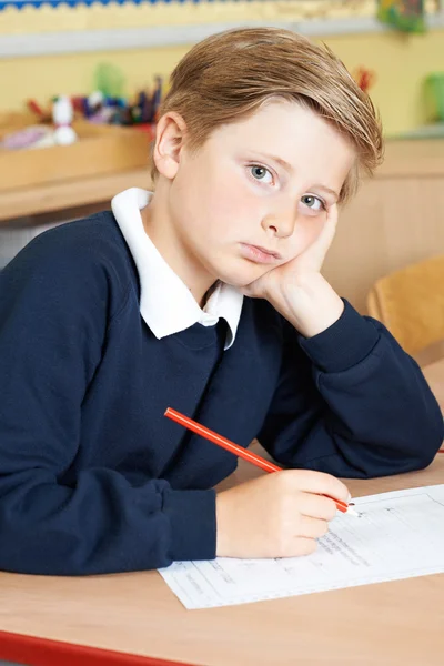 Gelangweilte männliche Grundschülerin am Schreibtisch — Stockfoto