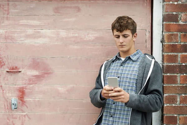 Adolescente menino mensagens no celular em configuração urbana — Fotografia de Stock