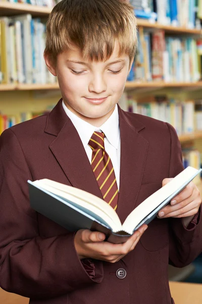 Αγόρι που φορούν σχολική ομοιόμορφη ανάγνωση βιβλίων στη βιβλιοθήκη — Φωτογραφία Αρχείου