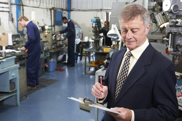 Inhaber einer Maschinenfabrik mit Mitarbeitern im Hintergrund — Stockfoto