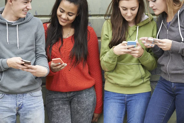 Groep tieners SMS-bericht op mobiele telefoons delen — Stockfoto