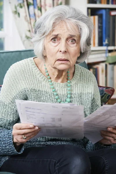 Äldre kvinna går igenom räkningar och ser orolig — Stockfoto