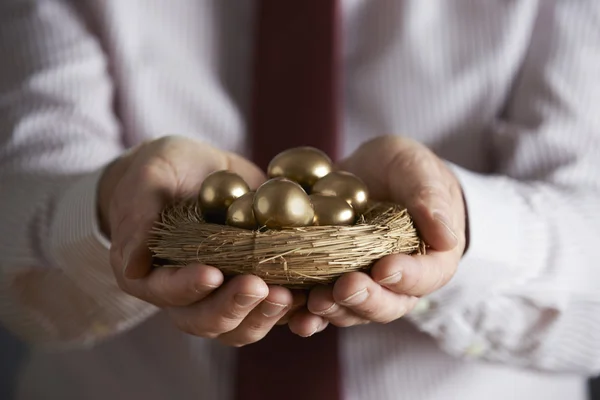 Empresario sosteniendo el nido lleno de huevos de oro — Foto de Stock