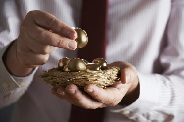 Бизнесмен держит гнездо, полное золотых яиц — стоковое фото
