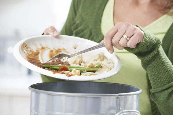 Женщина скребает остатки еды в мусорный бак — стоковое фото