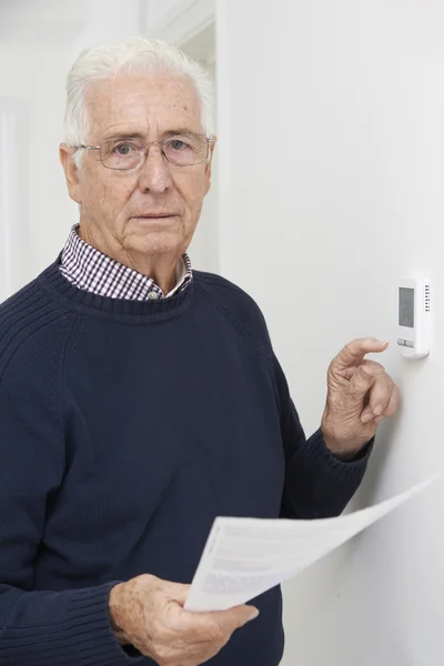 Worried Senior Man With Bill Turning Down Central Heating Thermo — Stock Photo, Image