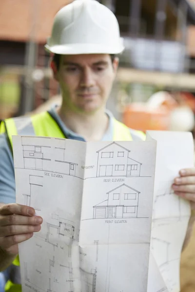 Trabajador de la construcción en el sitio de construcción mirando los planes de la casa —  Fotos de Stock