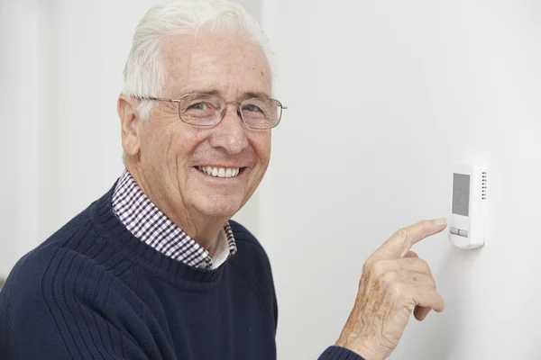 Hombre mayor sonriente que ajusta el termostato de calefacción central —  Fotos de Stock