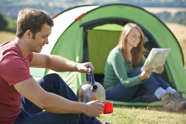 Casal fazendo bebida quente enquanto acampando no campo — Fotografia de Stock