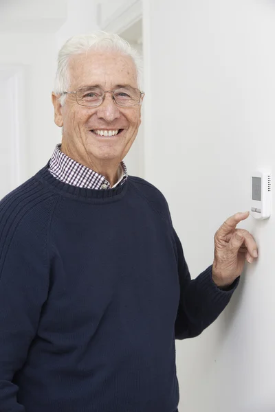 Uomo anziano sorridente che regola il termostato del riscaldamento centrale — Foto Stock