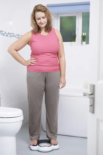 Obézní žena sama váží na vahách v koupelně — Stock fotografie