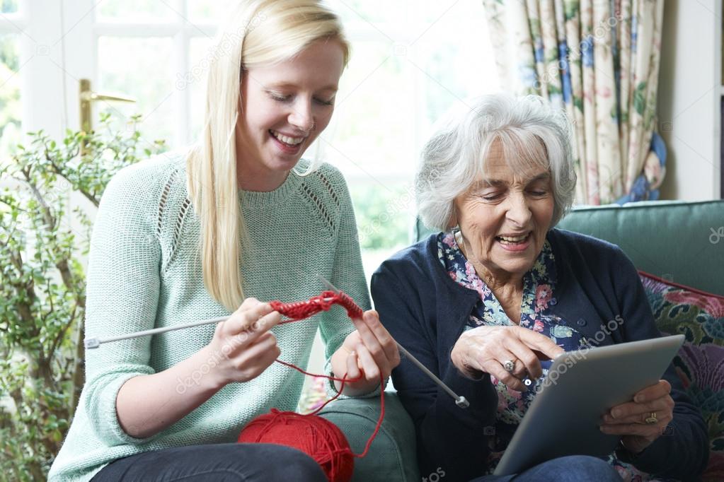 Grandmother Using Digital Tablet Whilst Granddaughter Knits 