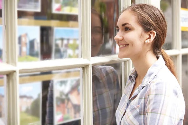 Sorridente giovane donna guardando nella finestra di agenti immobiliari — Foto Stock