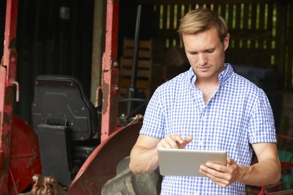 Agricultor segurando tablet digital em pé no celeiro com moda antiga — Fotografia de Stock