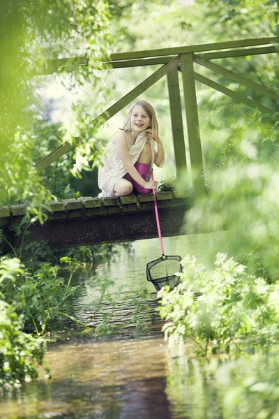 Молодая девушка ловит рыбу сетью с деревянного моста — стоковое фото