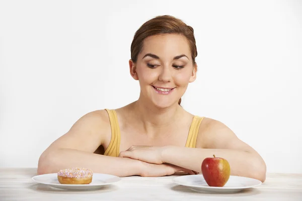 Mujer joven eligiendo entre rosquilla y pastel para merienda —  Fotos de Stock